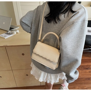 Detail of a beige woven PU crossbody bag with elegant handle and gold-tone hardware detail