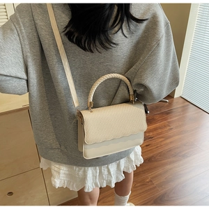 Chic cream handbag with woven texture flap shown on a model in a cozy interior setting