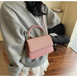 Chic pink crossbody bag with woven flap detail shown in a stylish indoor setting