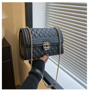 Detail of black quilted leather shoulder bag featuring a gold square lock and chain strap