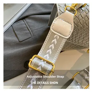 Detail of adjustable woven shoulder strap with gold buckle on gray embossed handbag