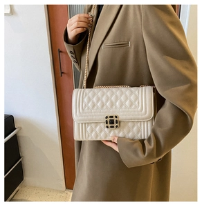 Detail of beige quilted shoulder bag with gold chain strap on a brown blazer outfit