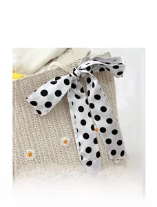 Detailed view of woven straw tote with white daisy embroidery and polka dot ribbon bow