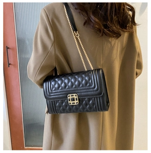 Detail of black quilted leather shoulder bag with gold square clasp and chain strap