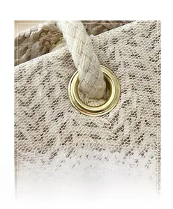 Detailed macro view of golden metal grommet and white lace mesh on woven straw tote