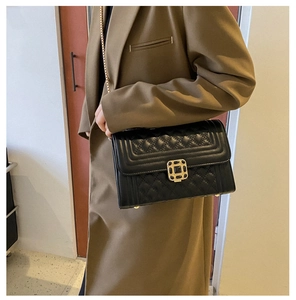Close-up of black quilted shoulder bag with vintage gold square buckle and chain strap