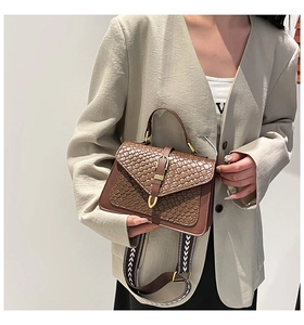 Detail of a brown woven crossbody bag with crocodile texture and geometric wide strap