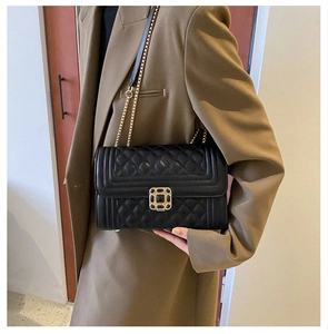 Detail of black quilted leather shoulder bag featuring a square gemstone lock and chain strap