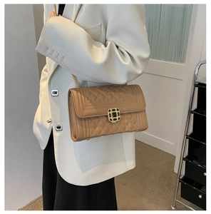 Close-up of quilted pattern and gold square lock with gemstone on camel chain crossbody bag