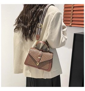Detail of a brown woven crossbody bag featuring a wide geometric pattern shoulder strap