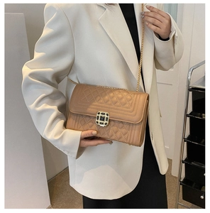Model wearing a beige quilted crossbody bag with gold chain strap and metal lock
