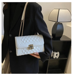 Close-up of a white quilted chain bag with a gold jewel-encrusted buckle on a black suit