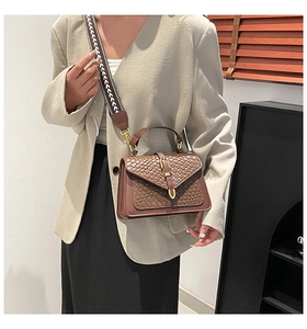 Detail of brown woven textured flap bag with bohemian wide strap and metal buckle