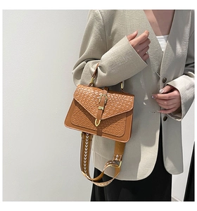 Detail of brown woven texture handbag with golden buckle and geometric strap on model
