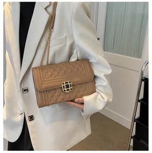 Detail of tan quilted shoulder bag with a gold rectangular lock and chain strap