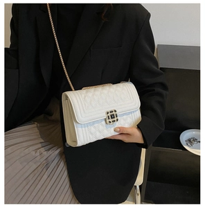 Detail of cream quilted crossbody bag with gold chain and black gemstone buckle on model