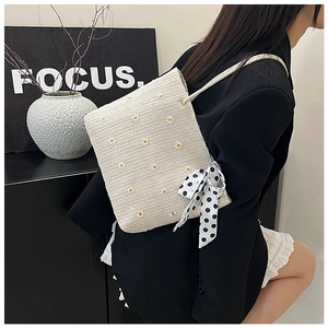Close-up of straw tote bag with daisy embroidery and a black polka dot ribbon bow
