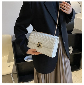 Close-up of white quilted crossbody bag featuring a golden chain strap and square lock