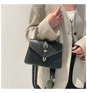 Detail of black woven texture handbag with gold buckle and geometric wide strap
