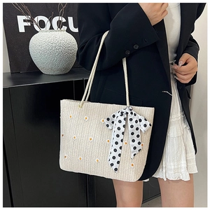 Detail of straw tote bag featuring daisy embroidery and polka dot silk scarf handle