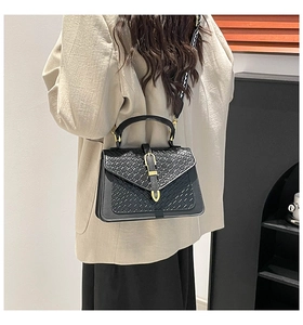 Detail of woven texture black crossbody bag with gold U-shaped buckle and patterned strap