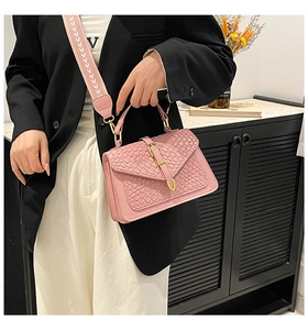 Detail of pink crossbody bag with woven flap, gold buckle, and patterned wide strap