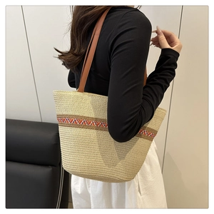 Detail of hand-woven straw tote bag with colorful geometric patterns and leather straps