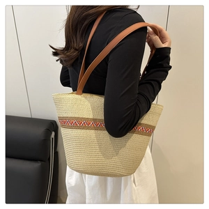 Detailed view of beige woven tote bag with ethnic patterned strap and leather handles