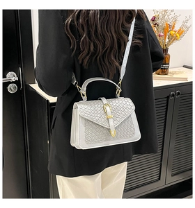 Detail of light grey crossbody bag with woven texture worn by model in black blazer