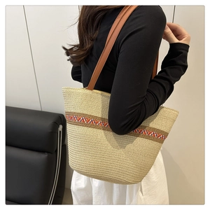 Detail of color-block woven straw tote bag featuring brown leather shoulder strap on model