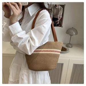 Detail of hand-woven straw shoulder bag with color-block stripes on a neutral background