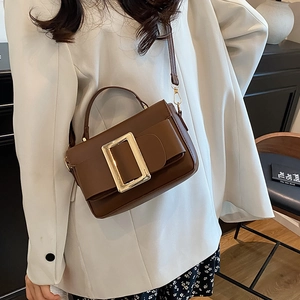 Brown matte leather crossbody handbag with a large gold buckle shown on a model in white