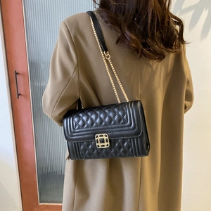 Chic black quilted crossbody bag with gold chain strap worn with stylish autumn coat