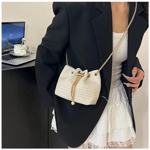 Detail of cream straw bucket bag featuring a gold chain and elegant pearl drawstring accents