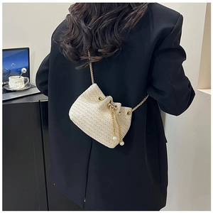Detail of cream woven bucket bag with elegant pearl drawstring and golden chain strap