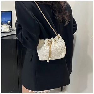 Detail of cream woven bucket bag with gold chain strap and pearl tassels on a model