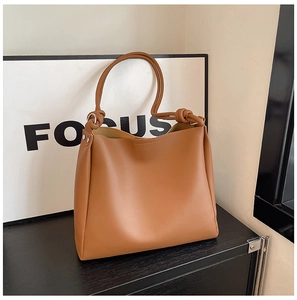 Détail d'un sac seau en similicuir marron avec anses nouées et rivets argentés chic