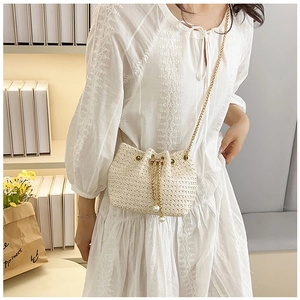 Detail of woven bucket bag with gold chain strap and pearl charm on white lace dress