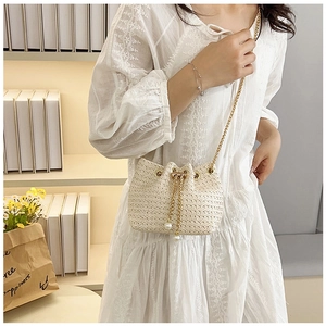 Detail of woven straw bucket bag featuring pearl drawstring accents and gold chain strap