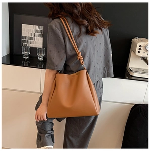 Détail d'un sac fourre-tout en cuir marron avec nœud décoratif sur la bandoulière et texture