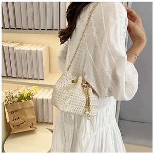 Close-up of woven bucket bag featuring gold chain and pearl tassel details on a model