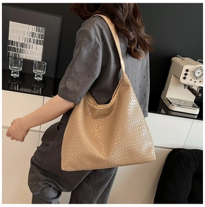 Detail view of large beige tote bag with snakeskin texture worn by model in cafe setting