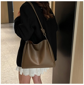 Sac seau en cuir vert olive avec bandoulière nouée porté par un mannequin en intérieur