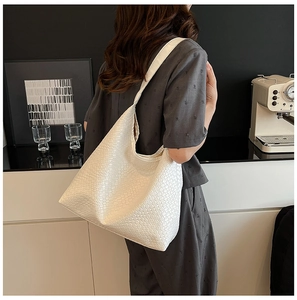 Detailed view of a white woven shoulder bag with wide strap on a model in a modern room