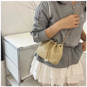 Detail of straw bucket bag featuring a gold chain strap and pearl drawstring accents