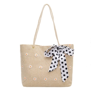 Woven straw tote bag with daisy embroidery and black polka dot bow on white background