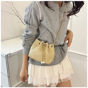 Detailed shot of woven straw bucket bag with pearl drawstring and gold chain strap