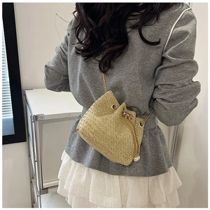 Detail of woven beige bucket bag with gold chain strap and pearl drawstring charms