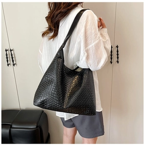 Detail shot of black woven tote bag with wide leather shoulder strap on model