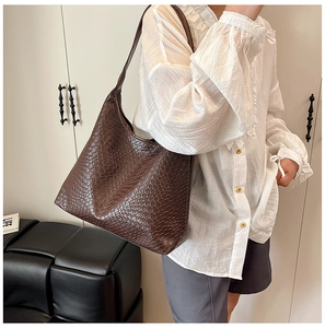 Close-up of a large dark brown woven pattern tote bag worn by a model in a casual setting